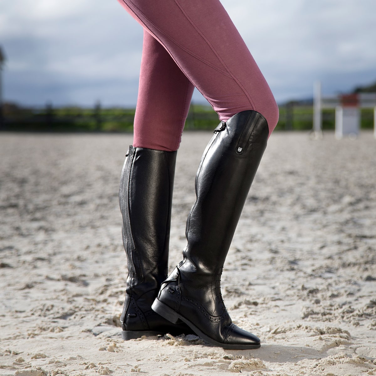 Woman wearing black tall boots and red breeches inside show jumping arena