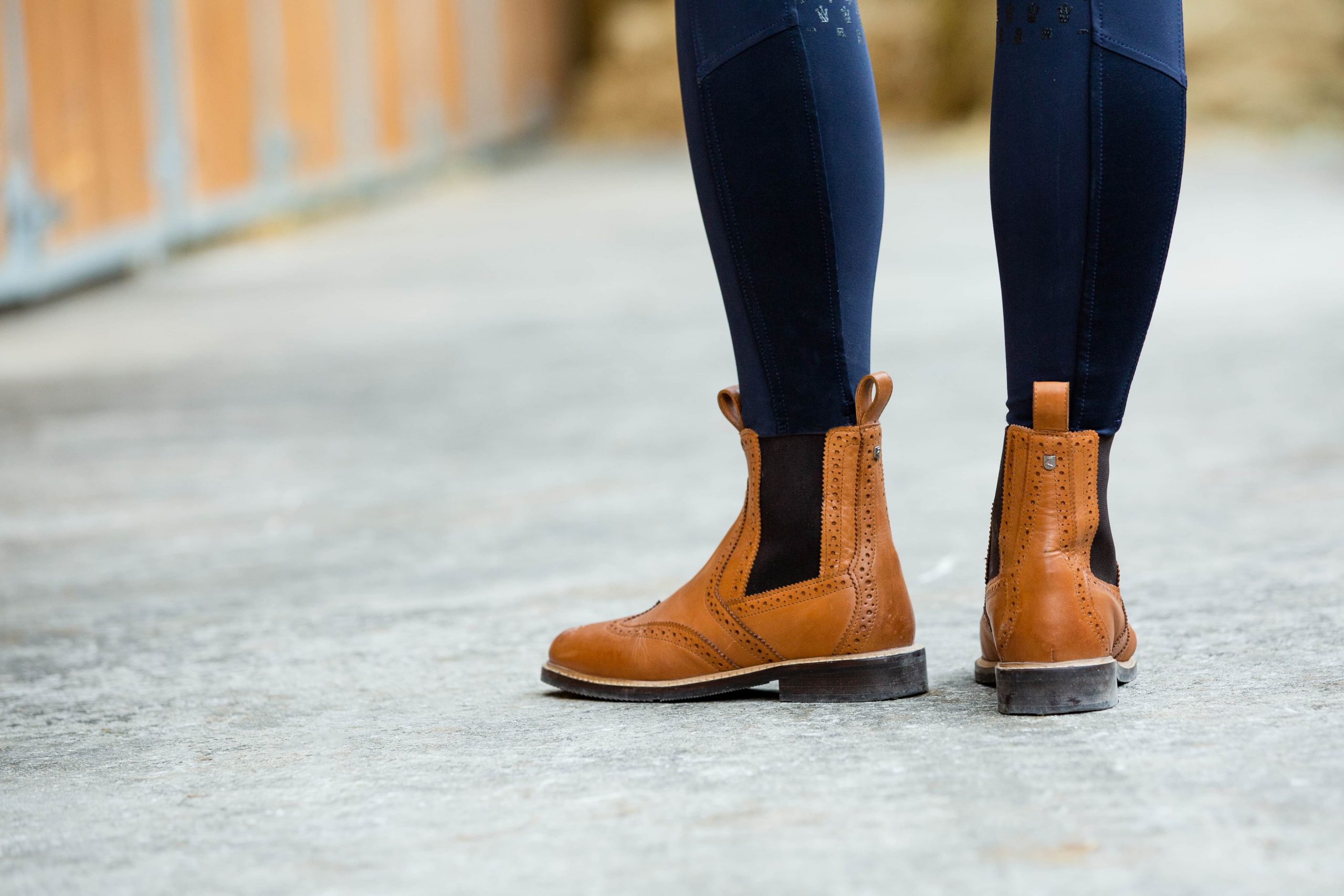 Woman standing outside stables wearing tan paddock boots